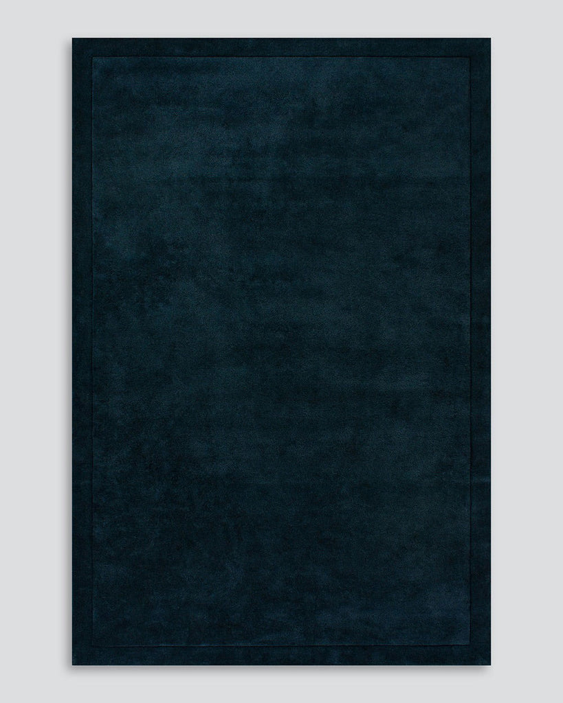 A full image of the Norfolk floor rug in the shade Ink. The border of the rug is cut-pile in a minimalist and refined design, and the pile of the rug's centre is luxuriously deep.
