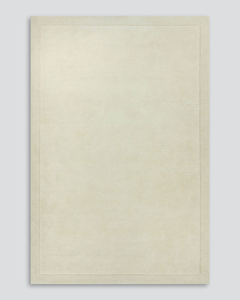 A full image of the Norfolk floor rug in the shade Ivory. The border of the rug is cut-pile in a minimalist and refined design, and the pile of the rug's centre is luxuriously deep.
