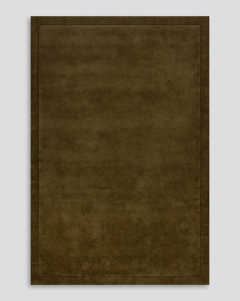 A full image of the Norfolk floor rug in the shade Olive. The border of the rug is cut-pile in a minimalist and refined design, and the pile of the rug's centre is luxuriously deep.
