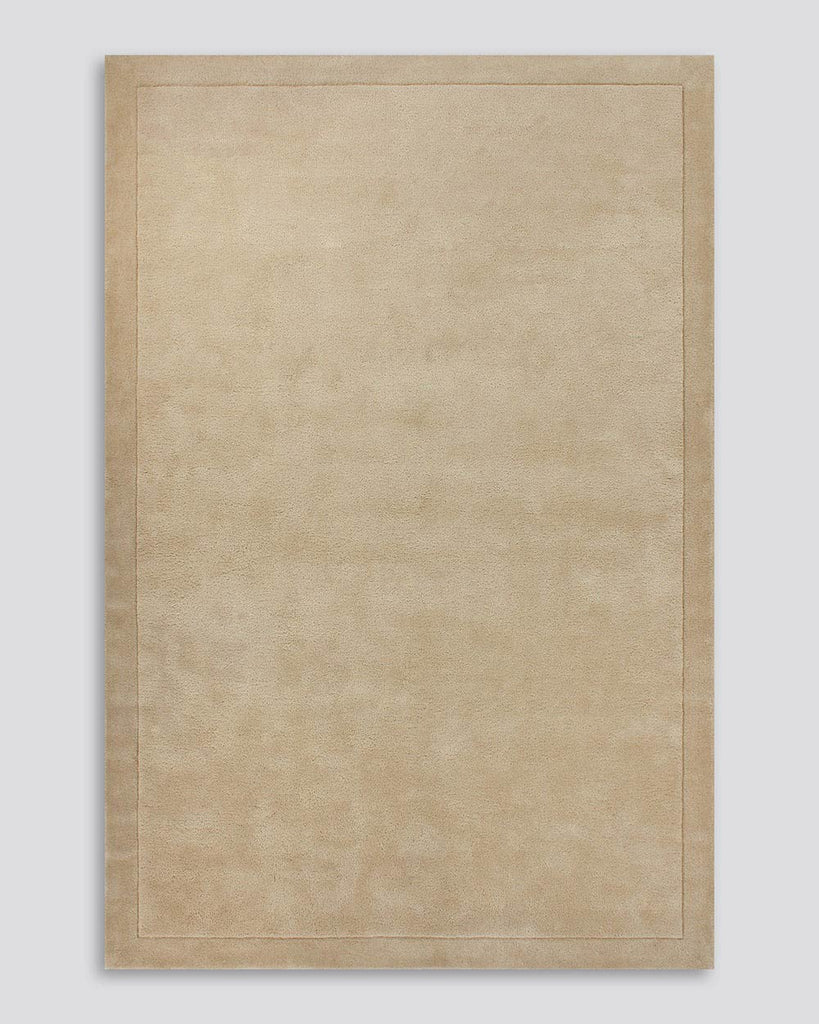 A full image of the Norfolk floor rug in the shade Sand. The border of the rug is cut-pile in a minimalist and refined design, and the pile of the rug's centre is luxuriously deep.
