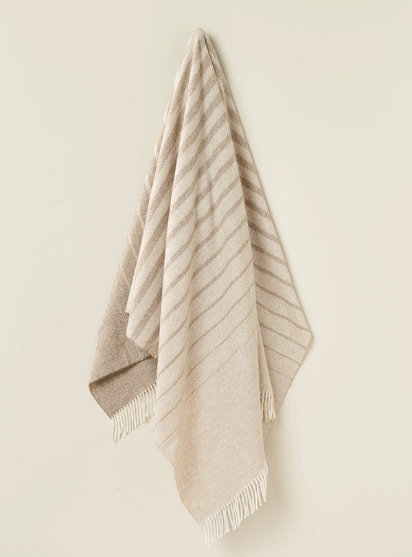 NZ merino wool throw blanket featuring a cream and beige stripe design, seen hanging with tassle fringe