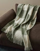 A green and white boucle wool throw blanket with fringe draped over a brown couch