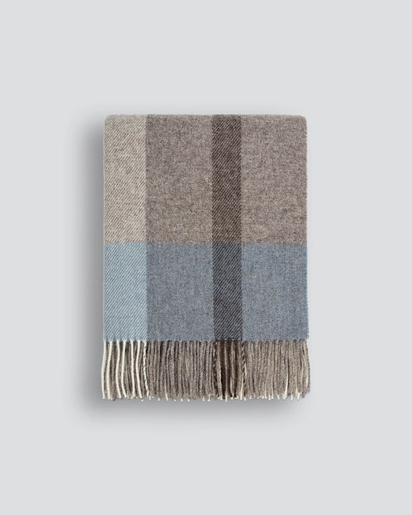The Baya nz wool throw blanket in soft blues and browns, with tasseled fringe