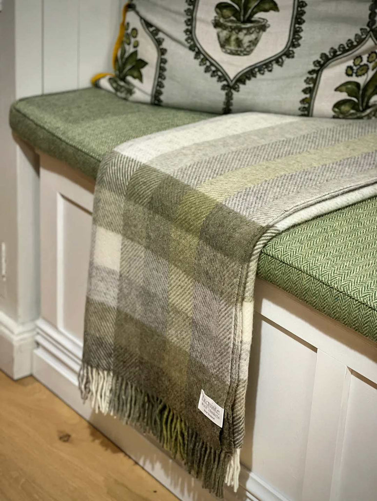 Pure nz wool throw blanket, by Exquisite Wool Traders, in olive green and white plaid shown folded on a window seat