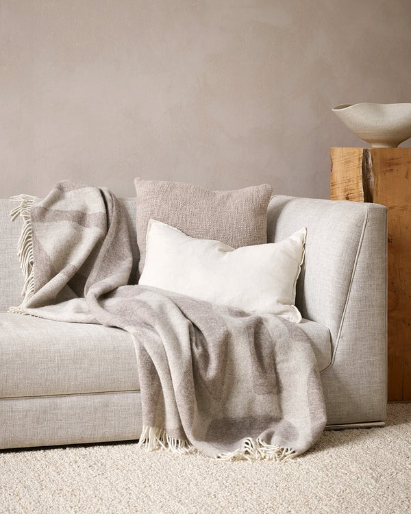 Baya 'Flagstone' NZ wool throw blanket in beige brown tones, draped on a couch in a contemporary home