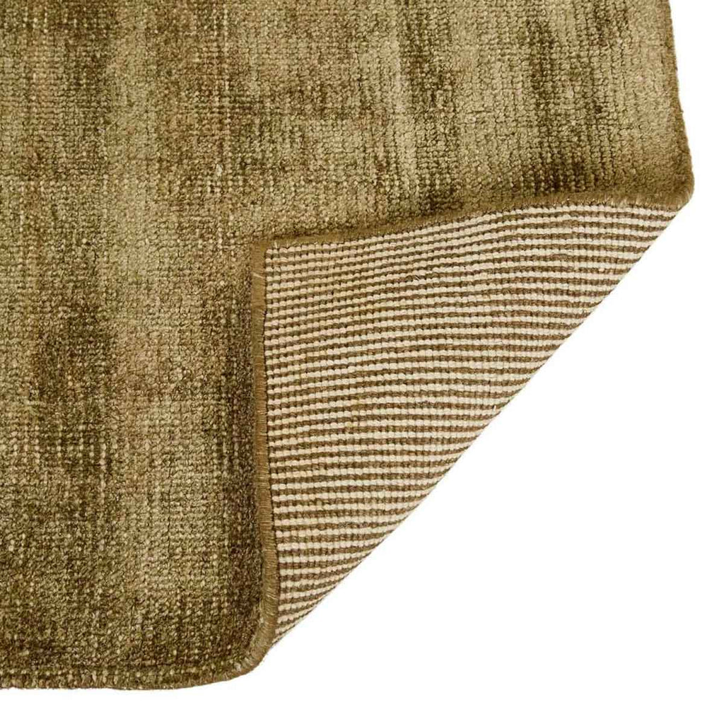 Close up of the corner of a soft, wool blend rug in shades of muted olive green by Soren Liv NZ and Globe West. The edge of the rug is flipped up to reveal the underside. 