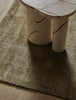 A soft, wool blend rug in shades of muted olive green by Soren Liv NZ and Globe West, on a wooden floor underneath a designer coffee table