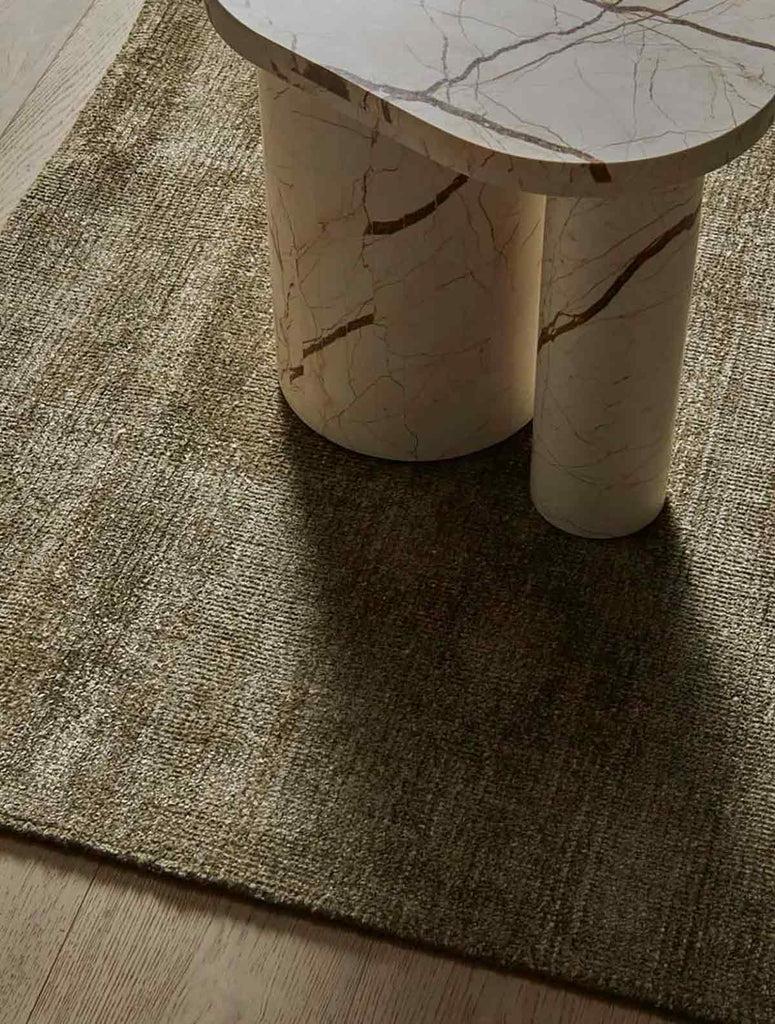 A soft, wool blend rug in shades of muted olive green by Soren Liv NZ and Globe West, on a wooden floor underneath a designer coffee table