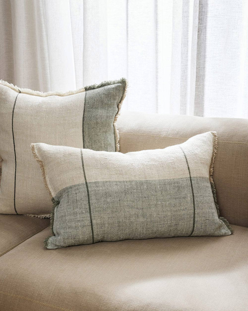 Two sage and cream toned linen cushions, one lumbar and one square, both with similar patterns of stripes and lines, and fringed edges.  By Baya