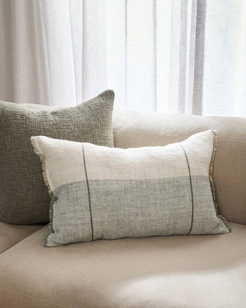 A cream couch with two linen cushions in shades of light sage and soft cream tones, the lumbar cushion in front decorated with parallel stripes and fringed edges. 