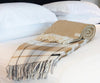 Palliser Ridge Twill Check lambswool throw in Mustard, draped over a bed showing the fringed edge, with another folded throw alongside