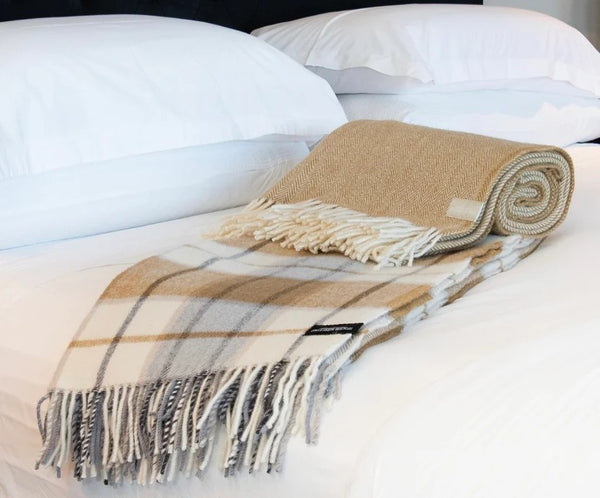 Palliser Ridge Twill Check lambswool throw in Mustard, draped over a bed showing the fringed edge, with another folded throw alongside