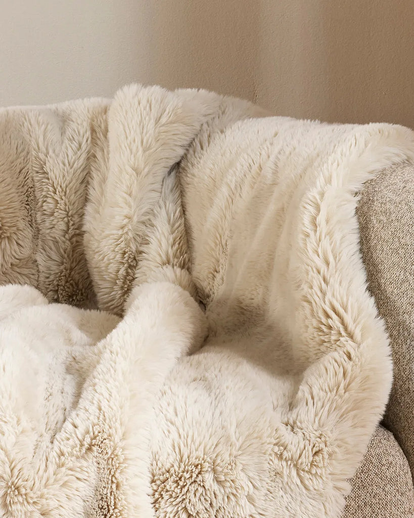 Soft, 'Pele' faux fur throw blanket, shown close up draped over a couch