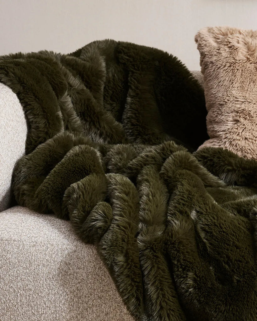 Pele Faux fur thrpow blanket by Baya, in a dark seaweed green colour, draped over a couch