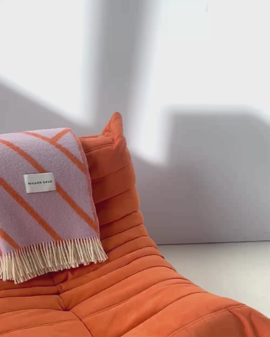 Maison Deux Lines wool throw in Lilac Orange, video of the throw being lifted from its box and unfolded on a table.