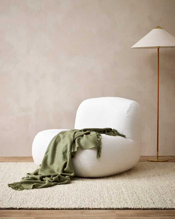 Moss green wool-blend throw blanket with tasseled fringe, draped over a chair in a contemporary living room