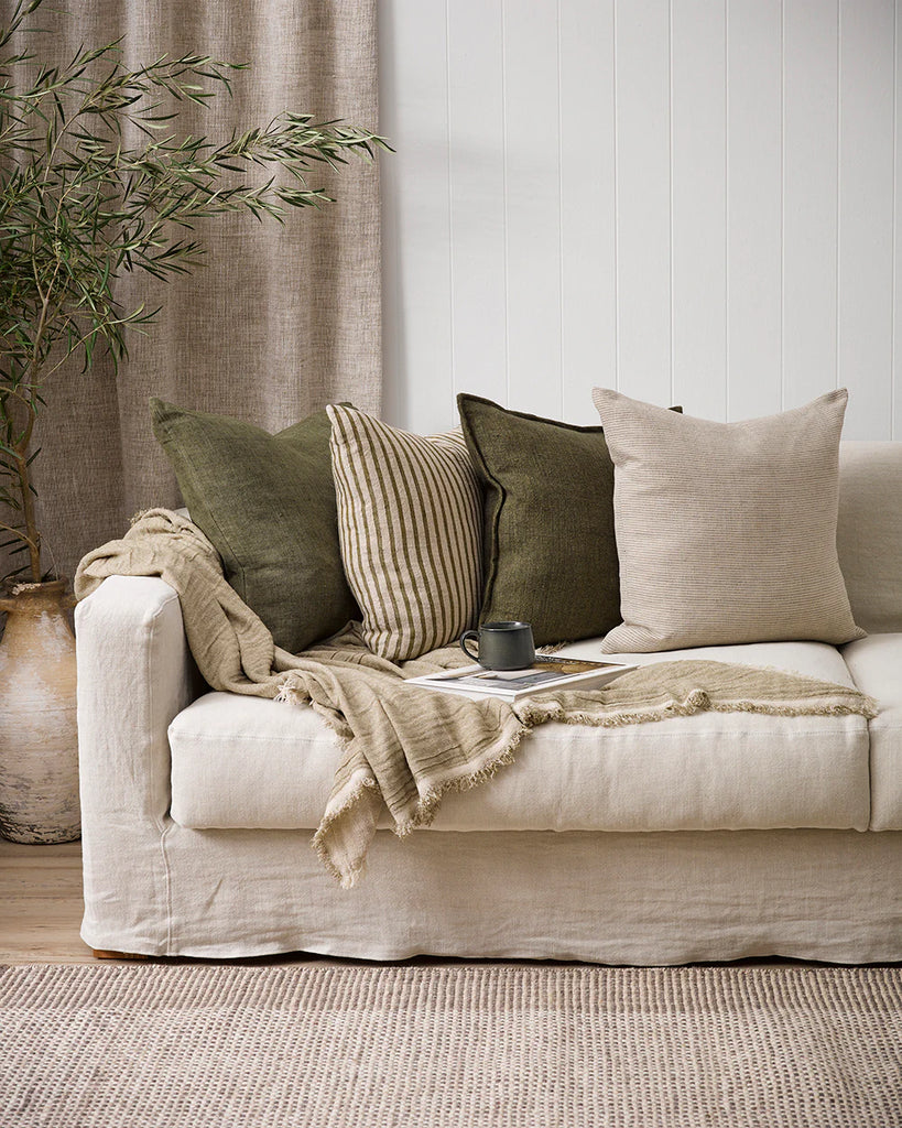 Four Baya designer cushions in complementary greens and neutral colours, on a cream couch