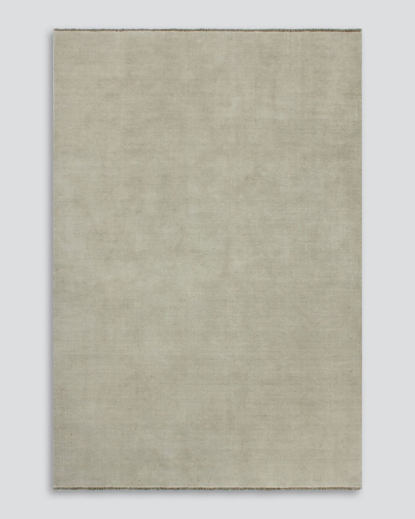 A full image of a soft grey-beige neutral floor rug in 100% wool with fringed edges by Baya. 