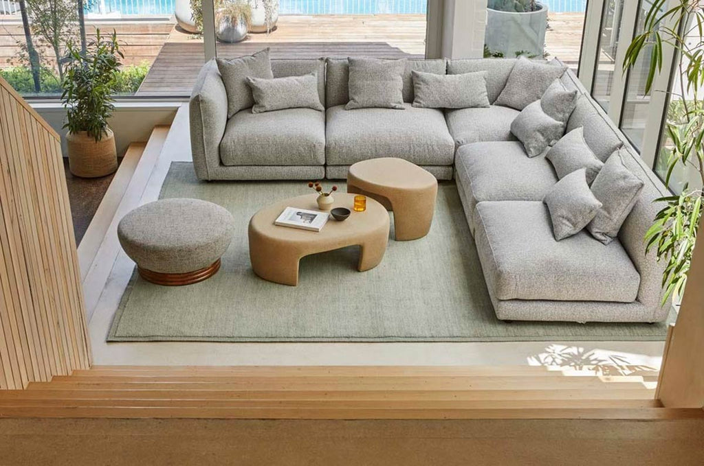 A handmade, 100% wool floor rug situated in a stylish living room by Soren Liv NZ and Globe West, in subtle shades of light blue and green, shades of seafoam. It has an indented border, giving interest and sophistication to the rug. 