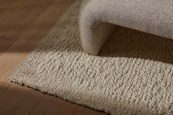 A textural wool blend boucle style rug by Globe West and Soren Liv NZ in shades of warm ivory and cream, situated underneath a designer couch. 