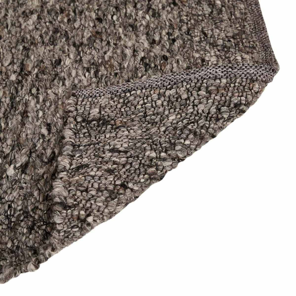 Close up of the weave of a textural wool blend boucle style rug by Globe West and Soren Liv NZ in shades of grey and charcoal. The edge is flipped over, showing the underside of the rug.