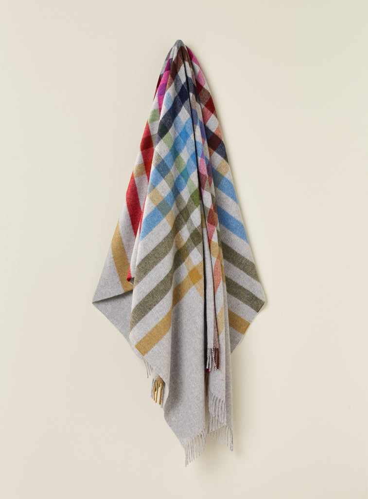 NZ wool throw blanket featuriing multi coloured stripes on a grey case