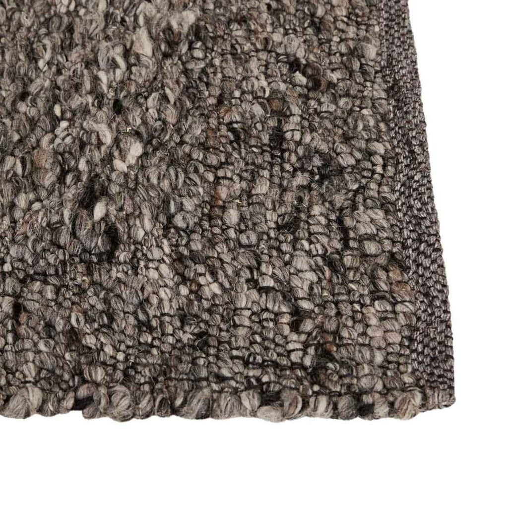 Close up of the corner of a textural wool blend boucle style rug by Globe West and Soren Liv NZ in shades of grey and charcoal. The edge is indented, adding interest. 