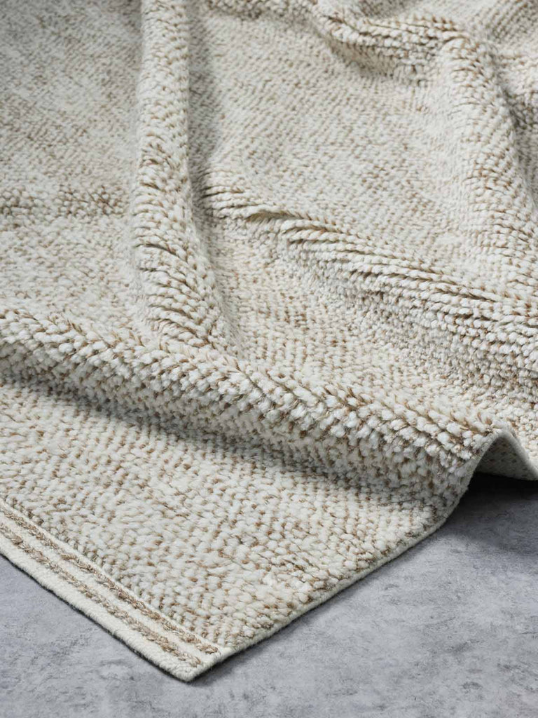 A luxurious, deep-cut pile floor rug in 100% NZ wool made by Tribe Home. A soft ivory colour offset with flashes of ginger, orange, and brown, with the depth of the pile offset by a linear border. 