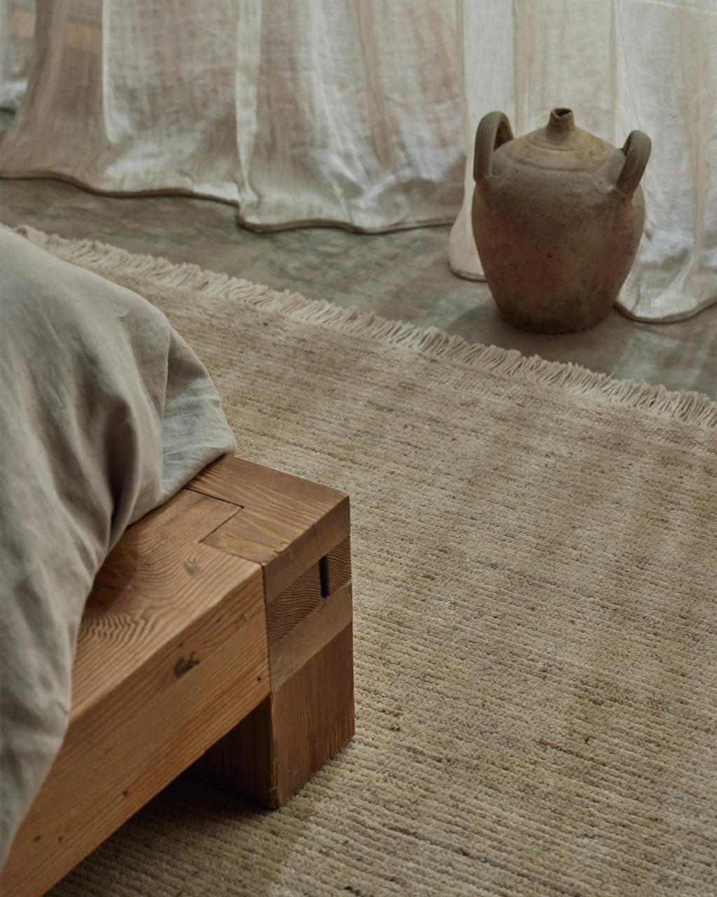 Weave Home Anton wool rug in Sand in a bedroom with a timber bench and a ceramic vessel