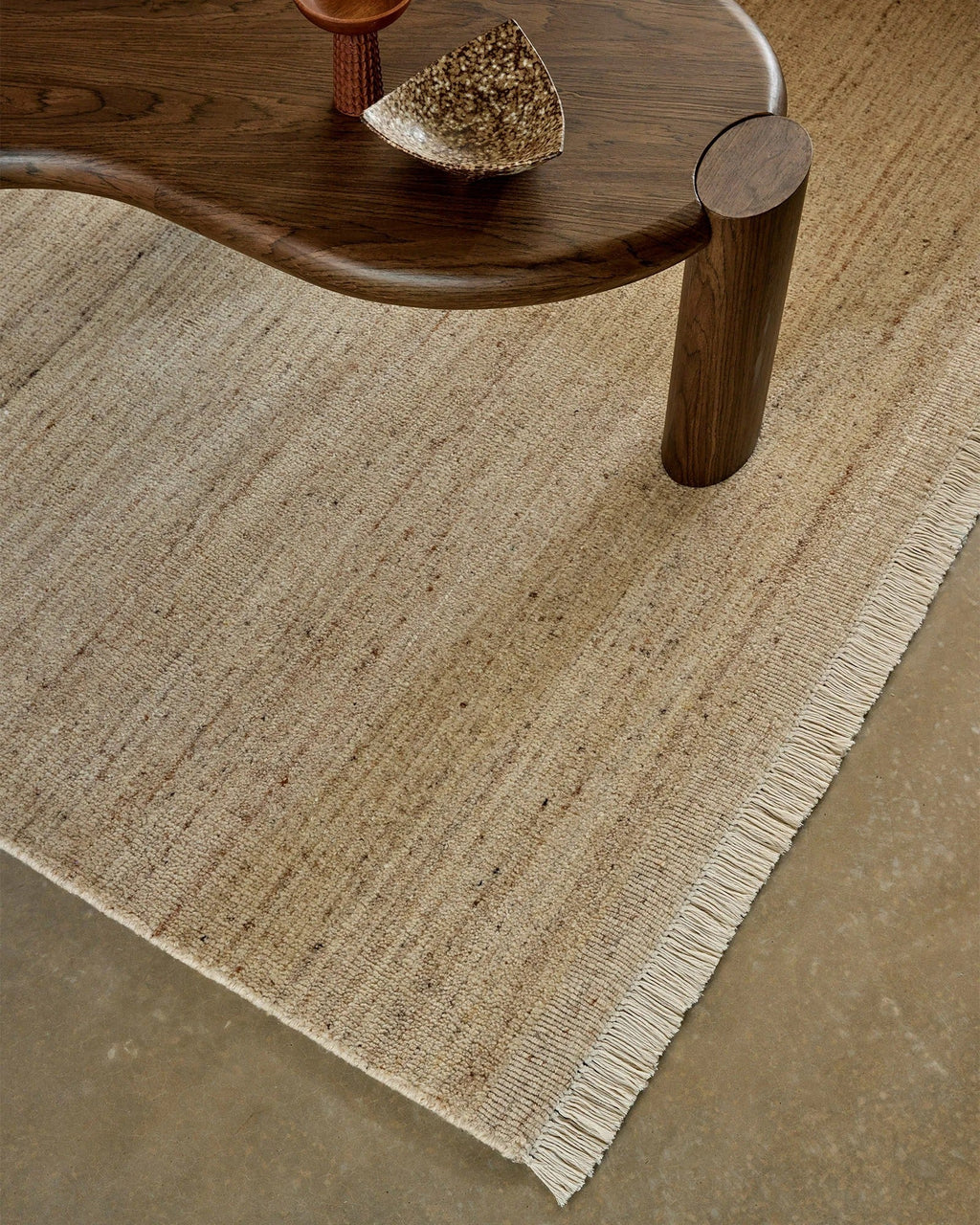 Weave Home Anton wool rug in Sand beneath a curved timber coffee table, close view of the pile and fringe