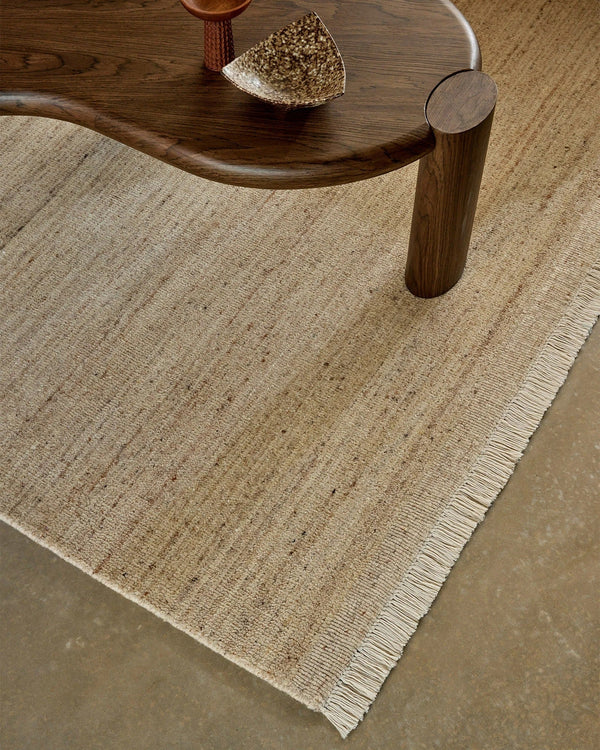 Weave Home Anton wool rug in Sand beneath a curved timber coffee table, close view of the pile and fringe