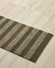 Weave Home Arden jute doormat in Coal on a timber floor beside a wooden dining chair.