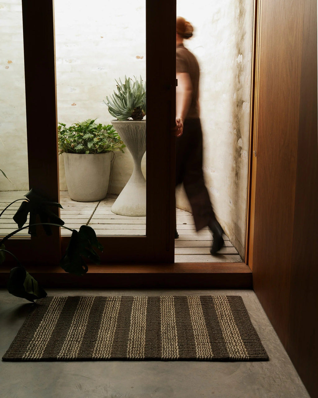 Weave Home Arden jute doormat in Coal at a home entryway, with a person walking through the doorway behind it.