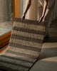A person holding the Weave Home Arden jute doormat in Coal up near a glass door.