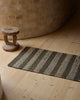 Weave Home Arden jute doormat in Coal styled on a timber floor next to a carved wooden stool.