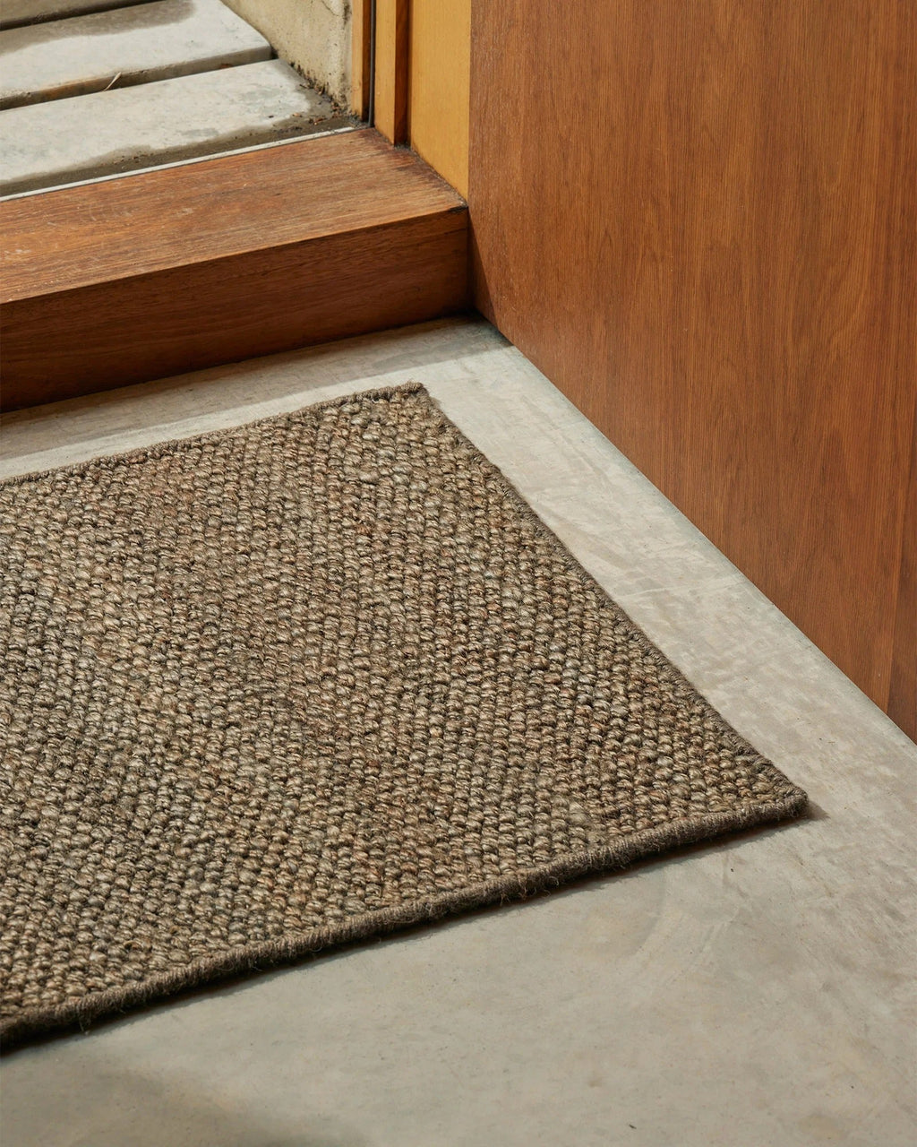 Weave Home Ivano jute doormat in Graphite at a concrete entrance step, close view.