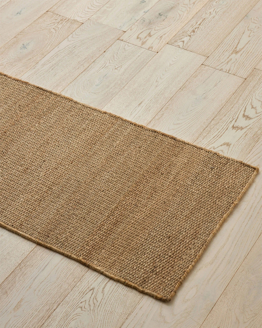 Weave Home Ivano jute doormat in Wheat, angled view on a herringbone wood floor.