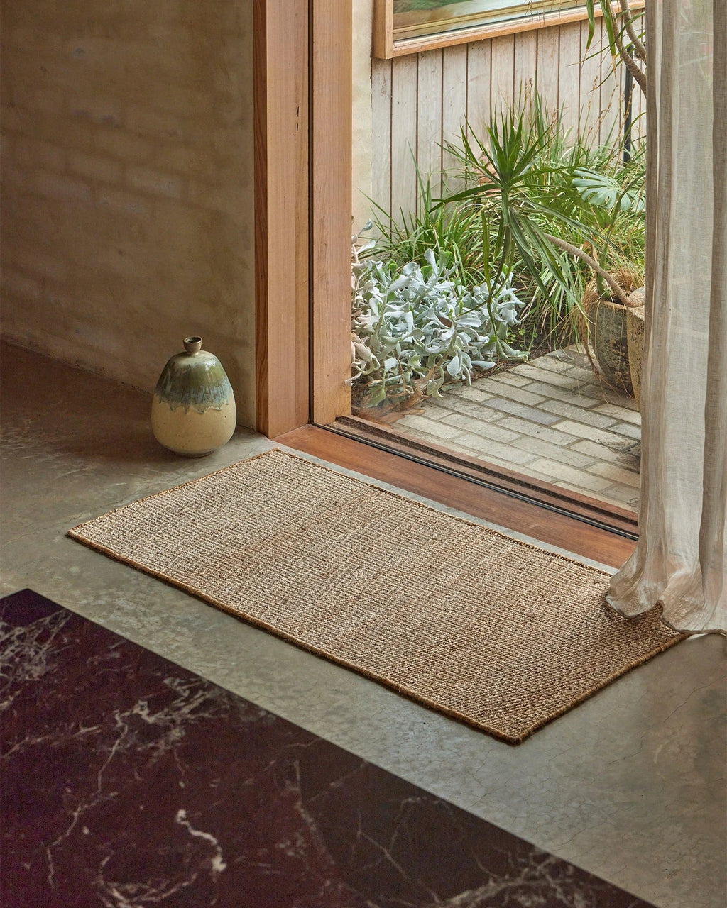 Weave Home Ivano jute doormat in Wheat styled at a timber entranceway.