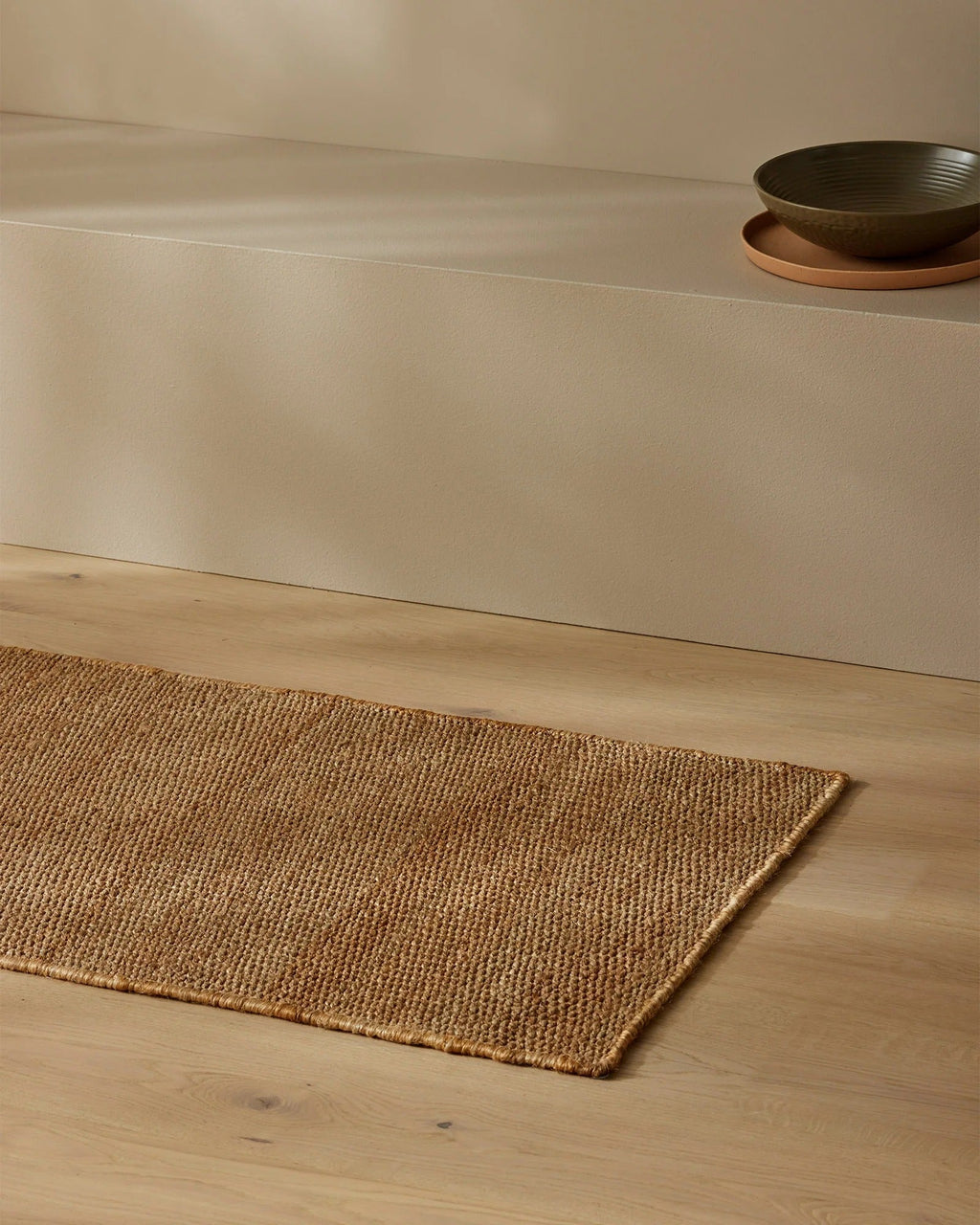 Weave Home Ivano jute doormat in Wheat, styled near a stone bench with a bowl and plate.