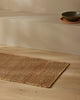 Weave Home Ivano jute doormat in Wheat, styled near a stone bench with a bowl and plate.