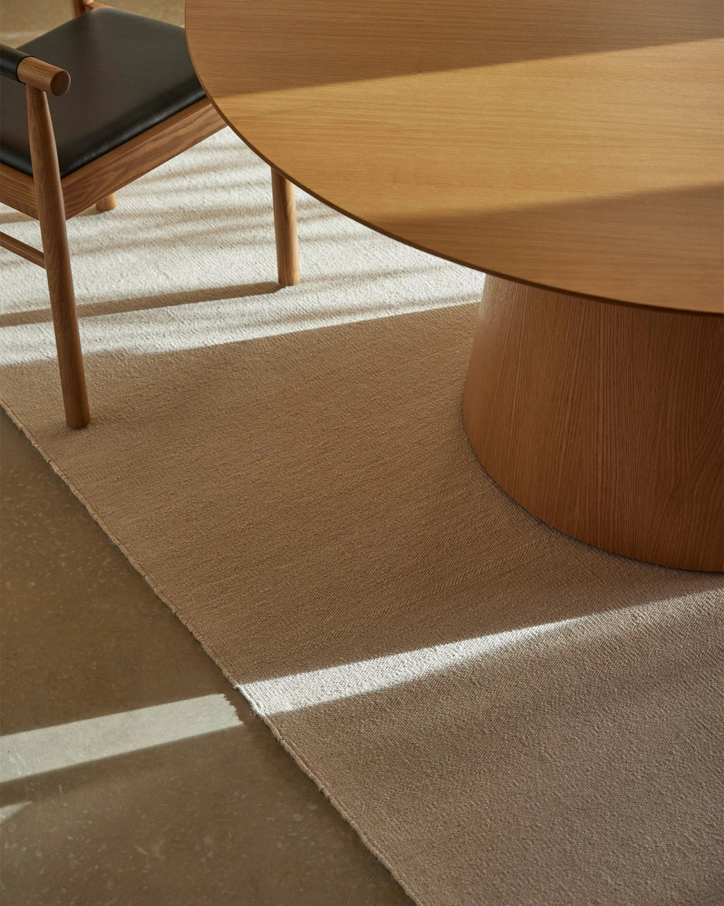 Weave Home Jacqueline wool rug in Cashew beneath a round timber table, with sunlight falling across the weave