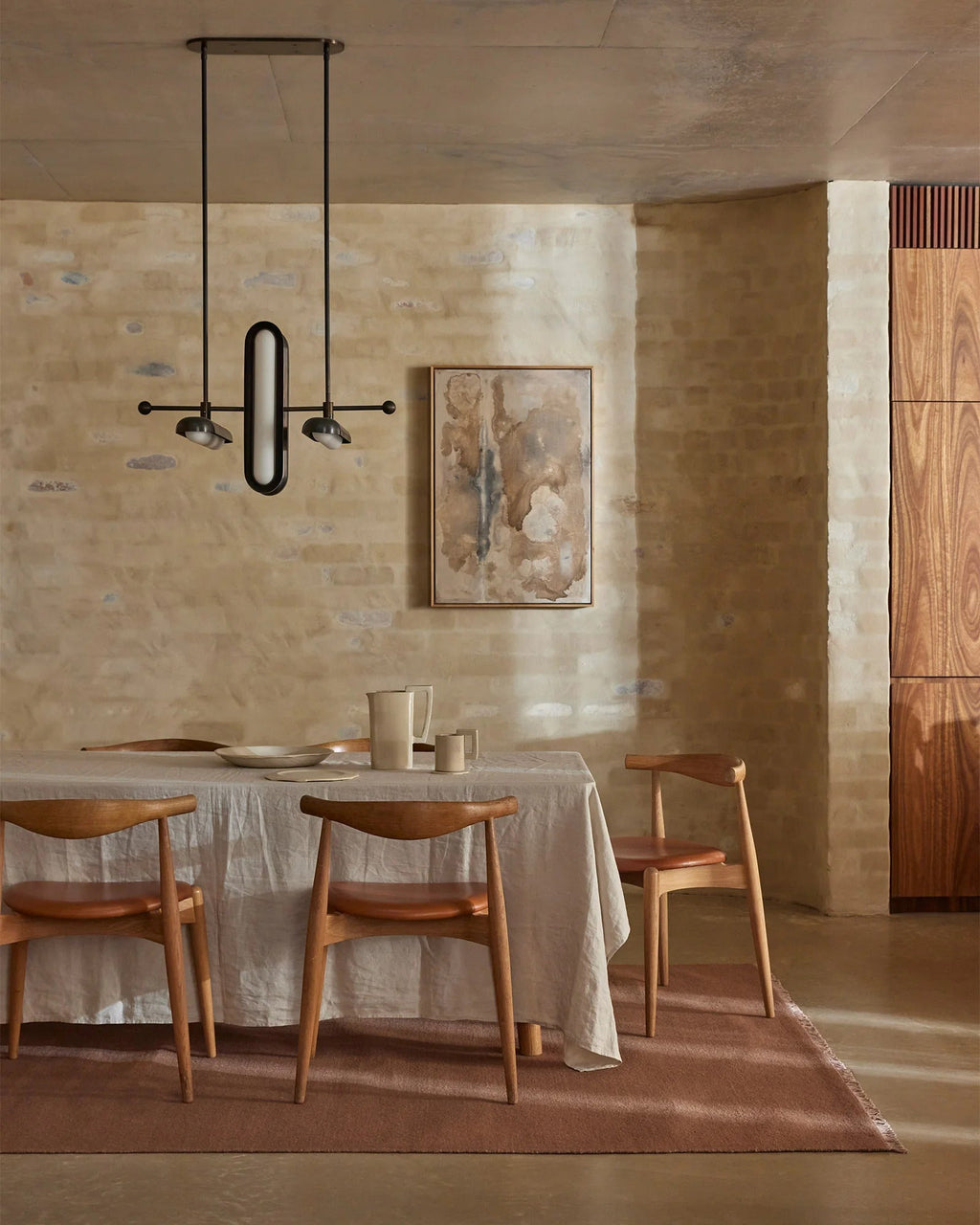 Weave Home Jacqueline wool rug in Rosewood in a dining room with limewashed brick walls and a pendant light