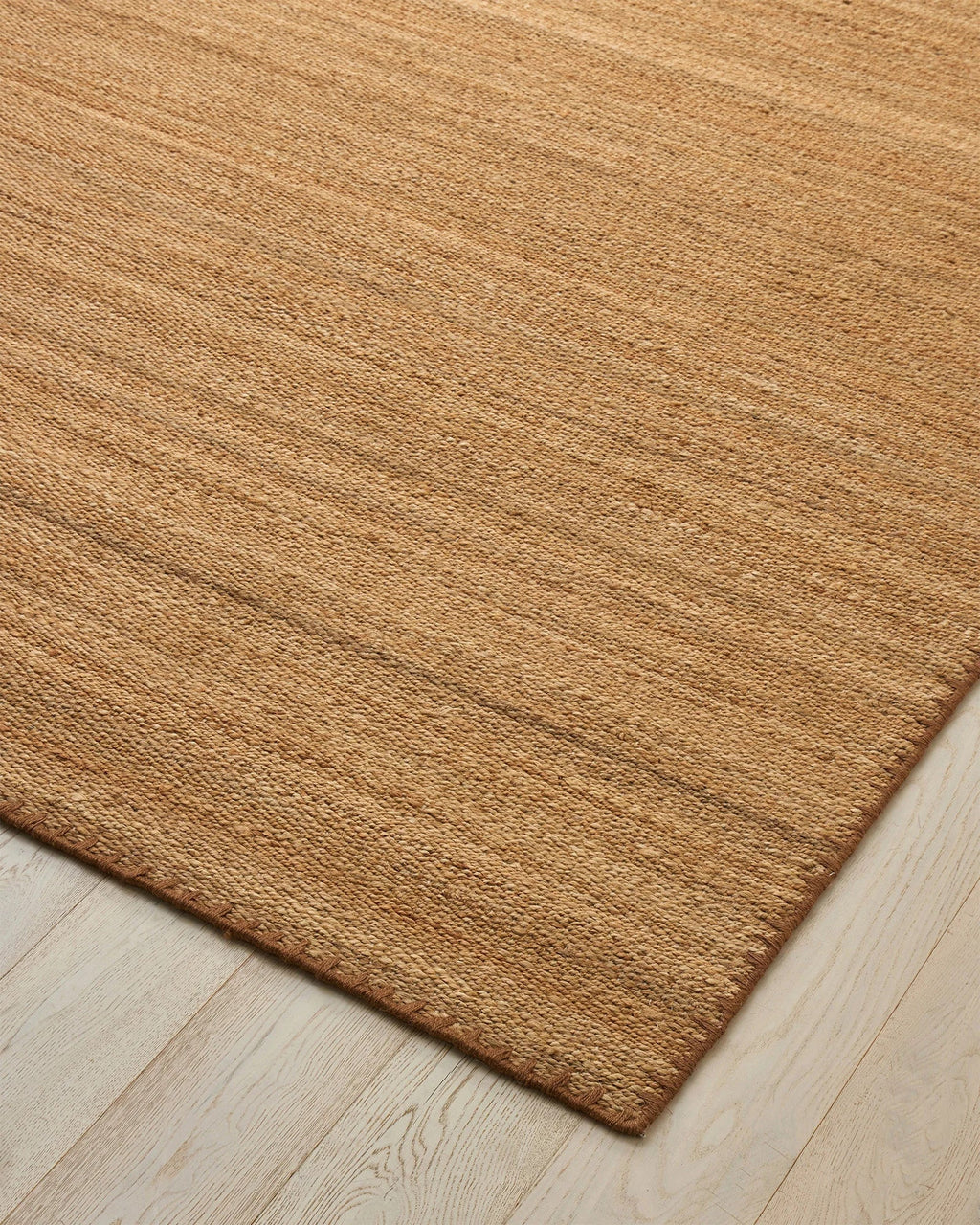 Weave Home Monroe jute rug in Biscuit on a pale timber floor, showing the stitched border and corner