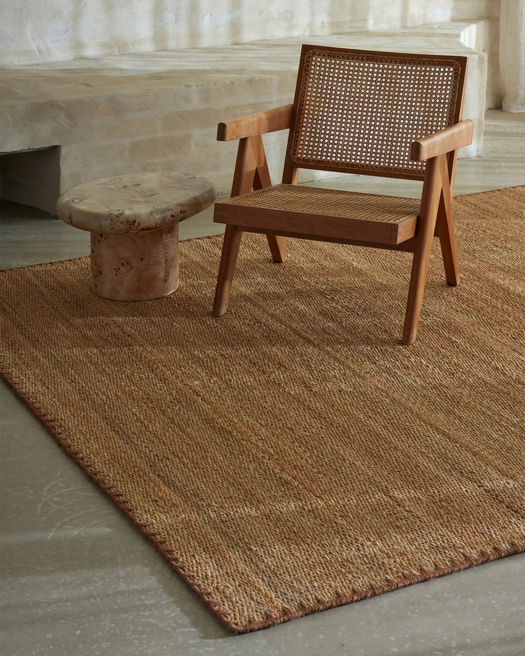 Weave Home Monroe jute rug in Biscuit with a cane armchair and a small burl side table