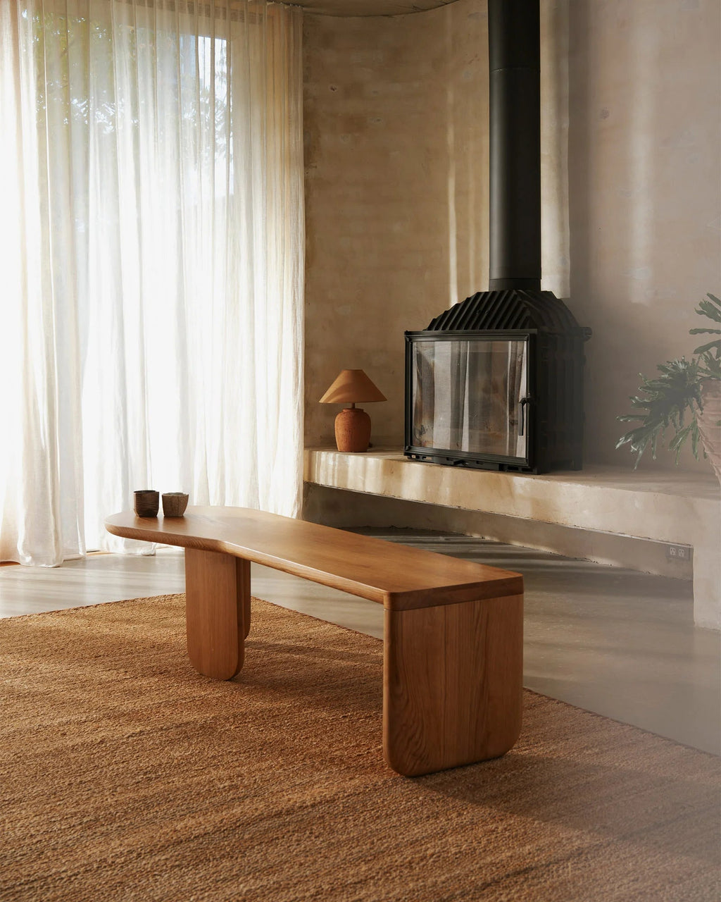 Weave Home Monroe jute rug in Biscuit in a living room with a curved timber bench and fireplace