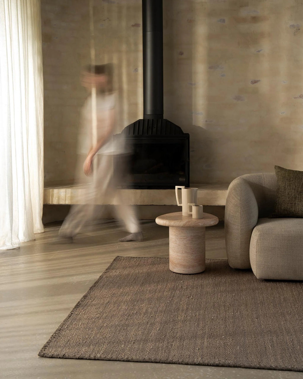 Weave Home Monroe jute rug in Flint beside a fireplace, with a stone side table and a linen sofa