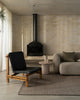 Weave Home Monroe jute rug in Flint in a living room with a black leather chair, a stone side table and a fireplace