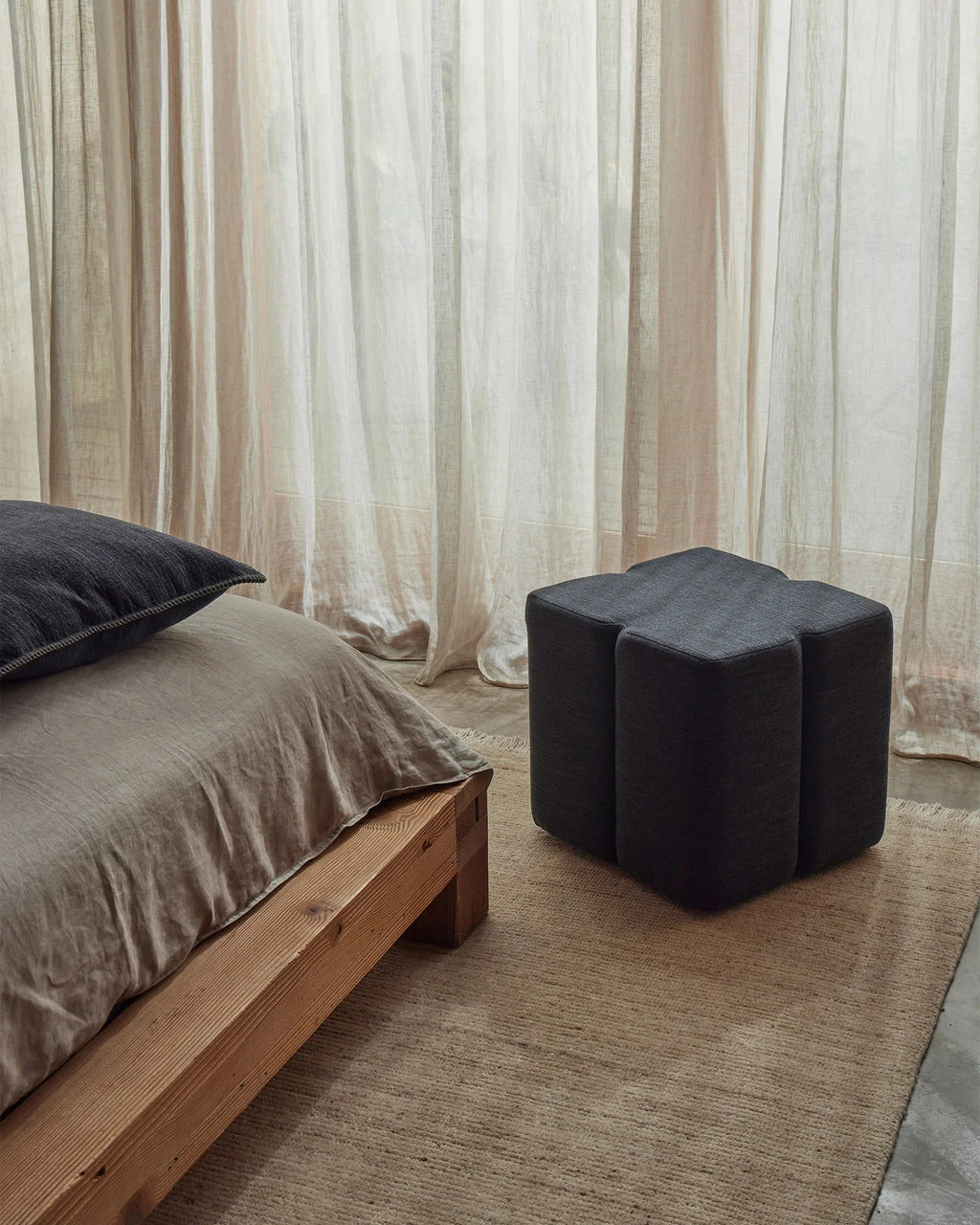 Weave Home Monroe jute rug in Oat in a bedroom with a timber bed and a dark upholstered stool