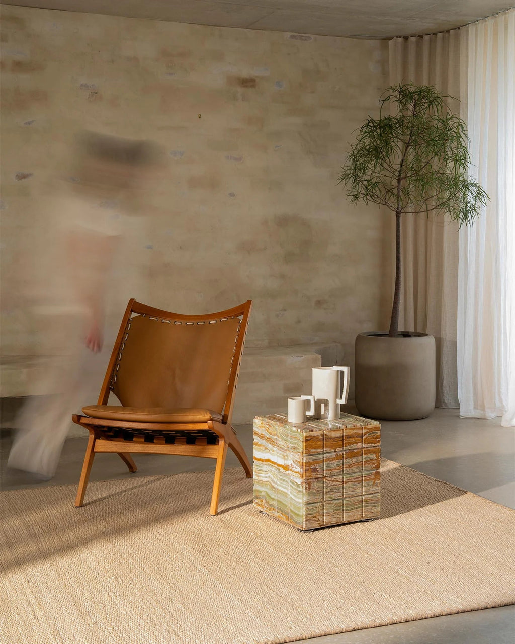 Weave Home Monroe jute rug in Oat in a living room with a leather sling chair and a stone cube table