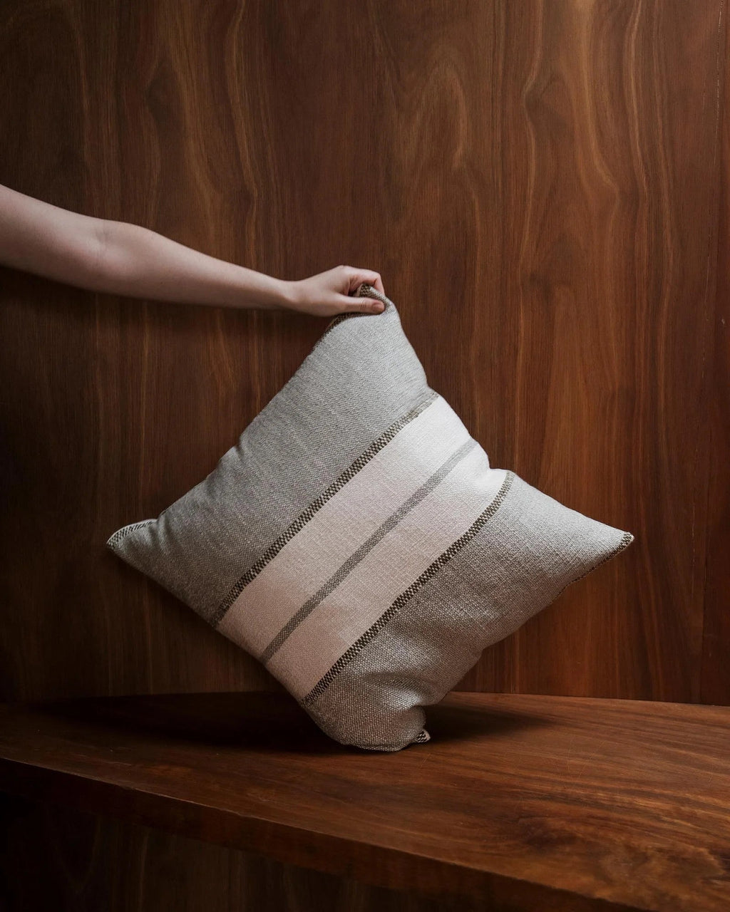 Weave Home Ottavio cushion in Lagoon held against a walnut-panelled shelf.